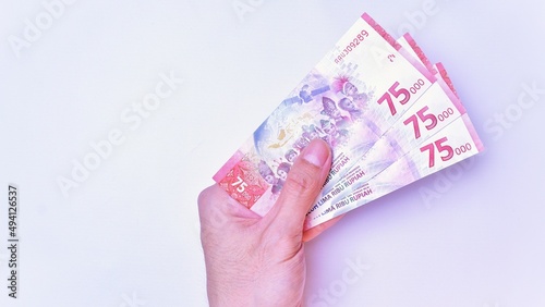 Indonesian Rupiah the official currency of Indonesia. Man's hand is making a payment. Male hand showing Indonesian Rupiah Note. Business Investment Economy and Finance Concept Uang 75000 75.000 Rupiah