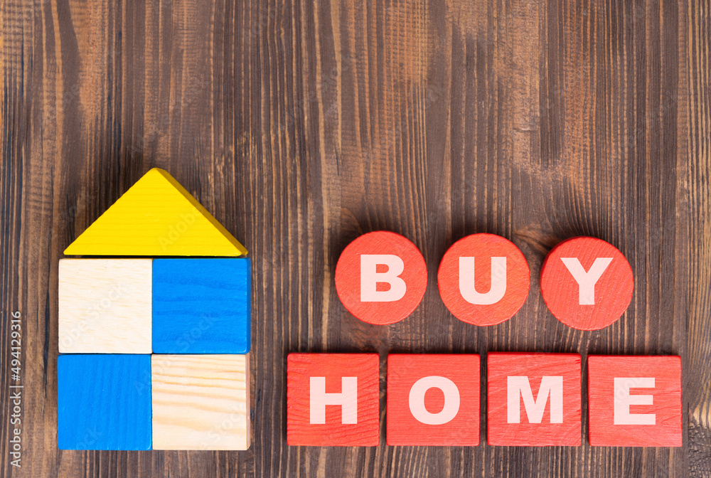 The concept of buying real estate. The phrase BUY HOME on red wooden cubes, a house made of wooden blocks on a brown background. The concept of buying real estate. The phrase BUY HOME on red wooden cubes, a house made of wooden blocks on a brown background.