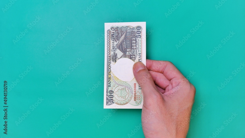 Indonesian Rupiah the official currency of Indonesia. Man's hand is making a payment. Male hand showing Indonesian Rupiah note. Business Investment Economy Loan and Finance concept. Uang 500 Rupiah Indonesian Rupiah the official currency of Indonesia. Man's hand is making a payment. Male hand showing Indonesian Rupiah note. Business Investment Economy Loan and Finance concept. Uang 500 Rupiah