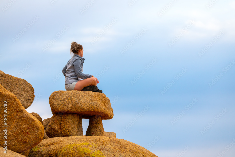 Woman tourist seen in Joshua Tree National Park waiting for sunset views over the desert landscape with bright blue sky background