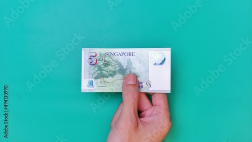Singapore Dollar is the official currency of Singapore. Business Investment Economy Money Income Loan and Finance concept. Businessman's hand showing Singapore Dollar on a green background. 5 Five SGD photo