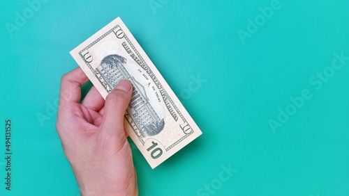Man's hand is making a payment. Business Investment Economy Money Loan Saving Income and Finance concept. Male hand showing dollar bills on green background. Ten Dollar. 10 USD. Prosperity concept.
