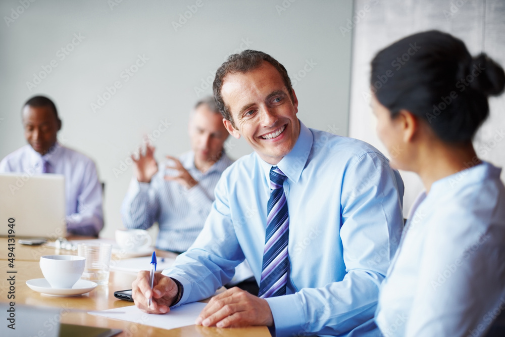 Two executives discussing proposal. Two executives in discussion with rest of team in background. Two executives discussing proposal. Two executives in discussion with rest of team in background.