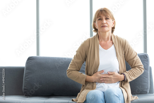 senior woman have a stomachache and holding stomach on sofa photo