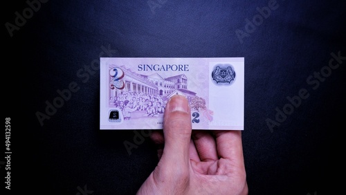 Singapore Dollar is the official currency of Singapore. Business Investment Economy Money Income Loan and Finance concept. Businessman's hand showing Singapore Dollar on a black background. 2 SGD.