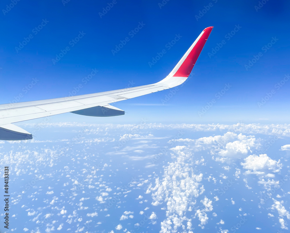 The sky outside the window on a domestic passenger plane. Airplane wings, clouds, and clear skies of a comfortable summer trip.