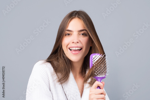 Happy smiling young woman combing hair. Portrait of female model with a comb brushing hair. Girl with hairbrush, hair care and beauty. Morning routine.