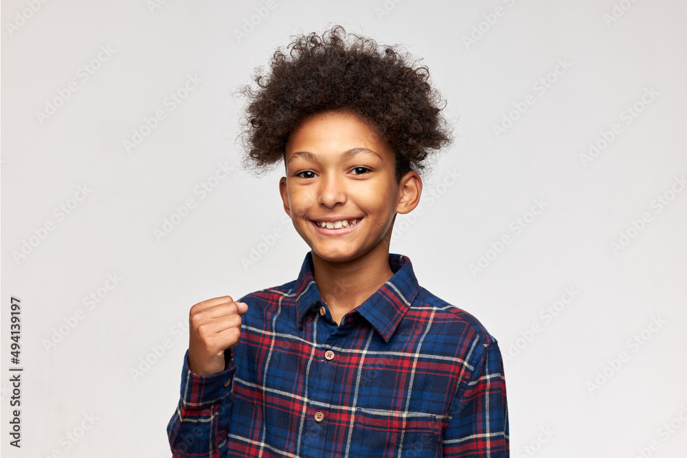 Studio shot of happy enthusiastic dark-skinned boy in flannel shirt showing yes sign with clenched fist, smiling isolated on white wall. Body language, gestures, emotions and feelings Studio shot of happy enthusiastic dark-skinned boy in flannel shirt showing yes sign with clenched fist, smiling isolated on white wall. Body language, gestures, emotions and feelings