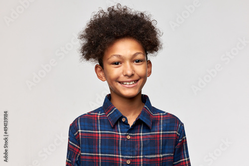 Portrait of cute adorable charismatic positive African American teen kid in blue shirt with toothy smile isolated against white studio wall with copy space for advertising content or text