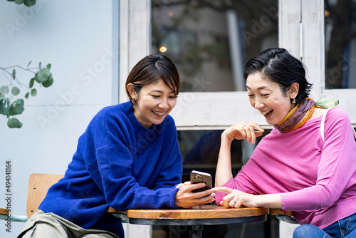 カフェテラスでスマートフォンを見るミドル世代の日本人女性2人