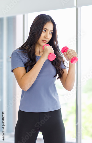 Asian young beautiful happy healthy female athlete sport girl in casual sporty outfit standing smiling holding small pink dumbbells in hands guarding learning practicing boxing exercise in classroom