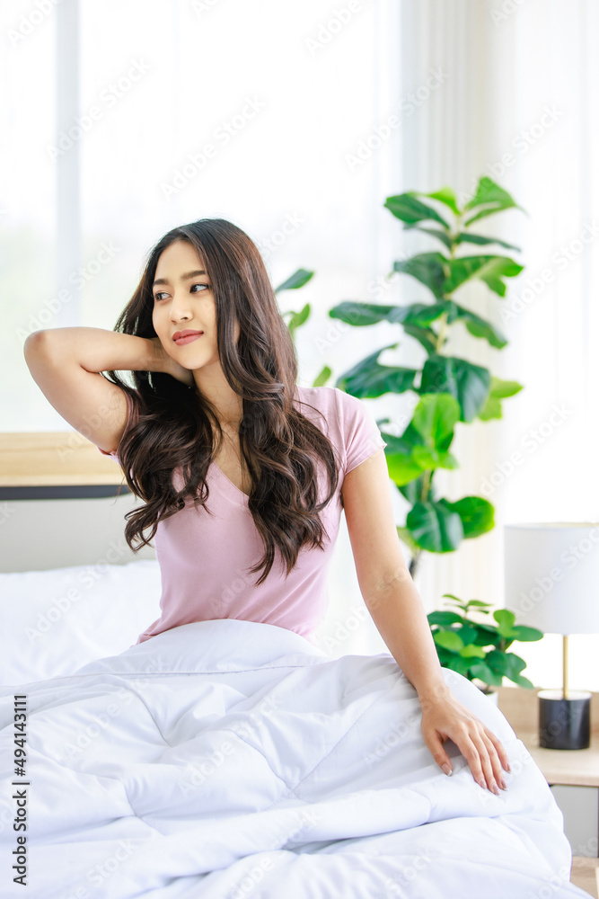 Asian young beautiful happy sleepy female teenager in casual pajama outfit waking up fresh in morning sitting smiling closed eyes under white blanket on bed in bedroom massaging stretching neck Asian young beautiful happy sleepy female teenager in casual pajama outfit waking up fresh in morning sitting smiling closed eyes under white blanket on bed in bedroom massaging stretching neck