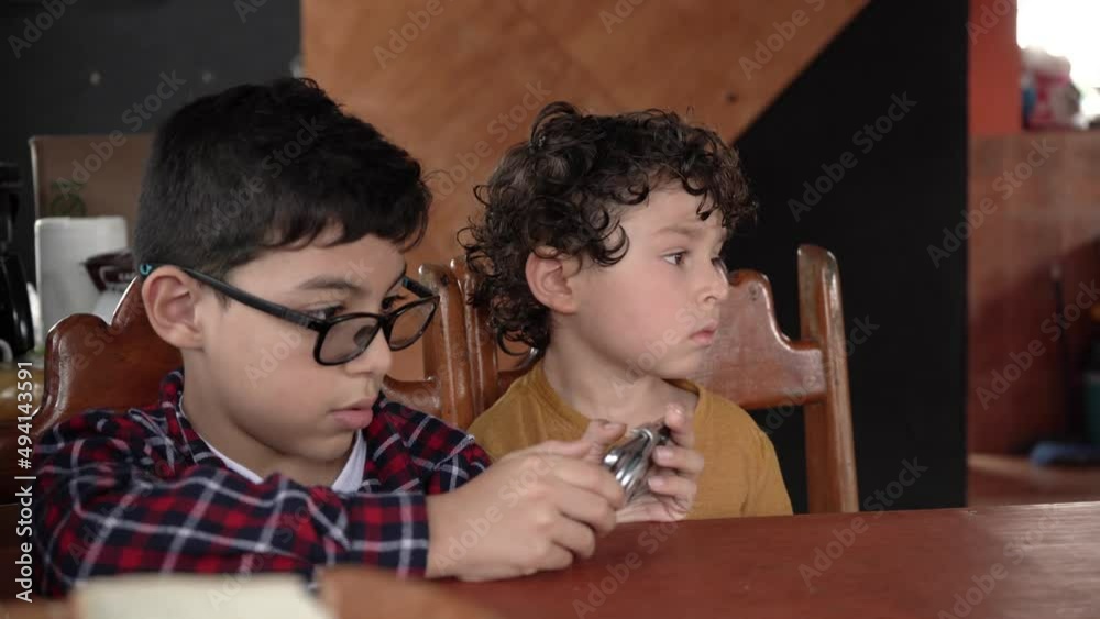Video of Latino kids sitting in the dining room using a cell phone at home