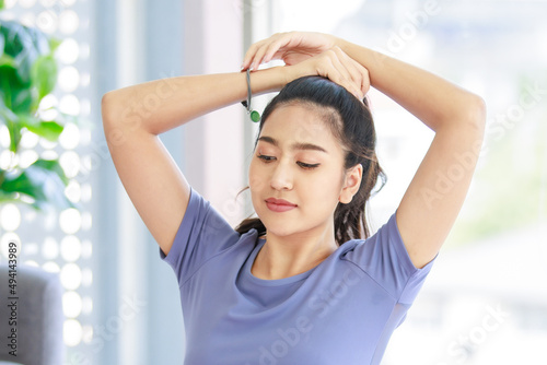 Asian young beautiful healthy athlete sport girl in casual sporty outfit sitting smiling on yoga mat holding hands tying long hair with elastic rubber band before exercising workout in living room