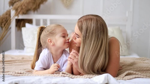 mom and daughter play, hug and kiss at home on the bed, lifestyle, tender relationship of a young mother and child, happy family and motherhood photo