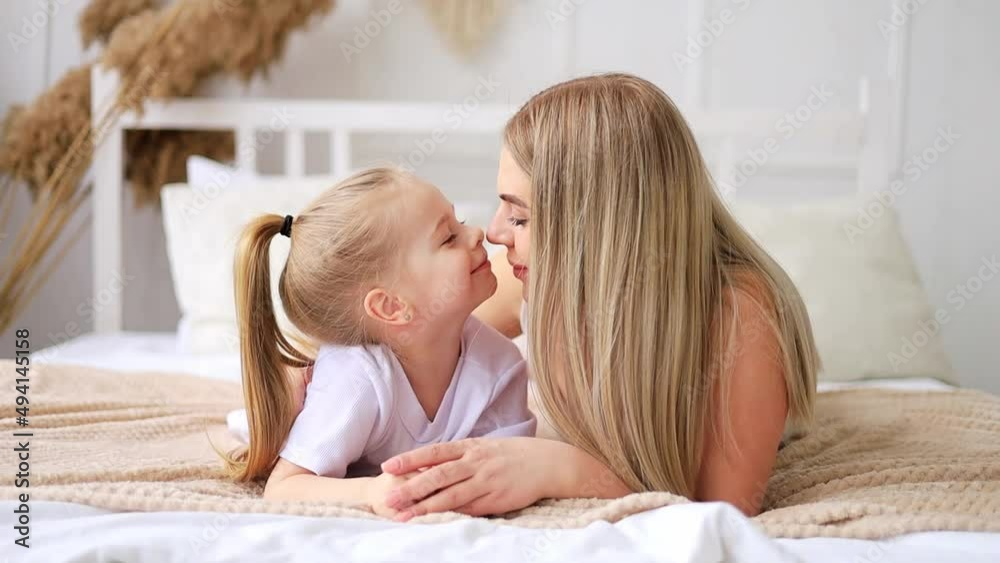 mom and daughter play, hug and kiss at home on the bed ...