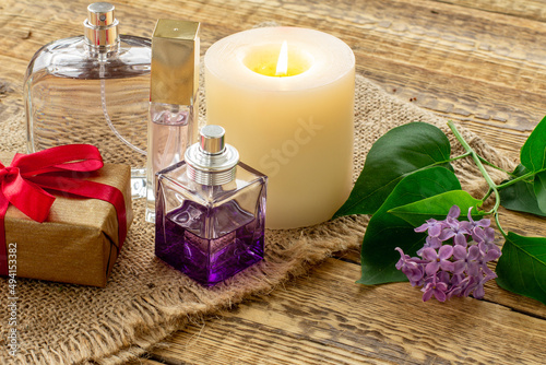 Bottles of perfume  candle and lilac flowers on wooden background.