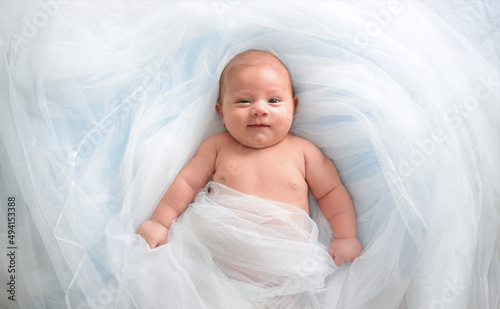 The baby lies on a white cloth and smiles, airy tulle, happy baby