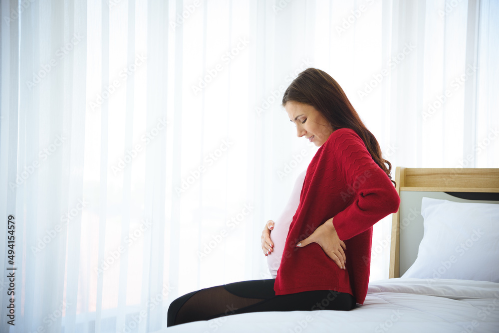 Pregnant woman sitting on bed and holding child in her belly in modern bedroom. Pregnant woman sitting on bed and holding child in her belly in modern bedroom.