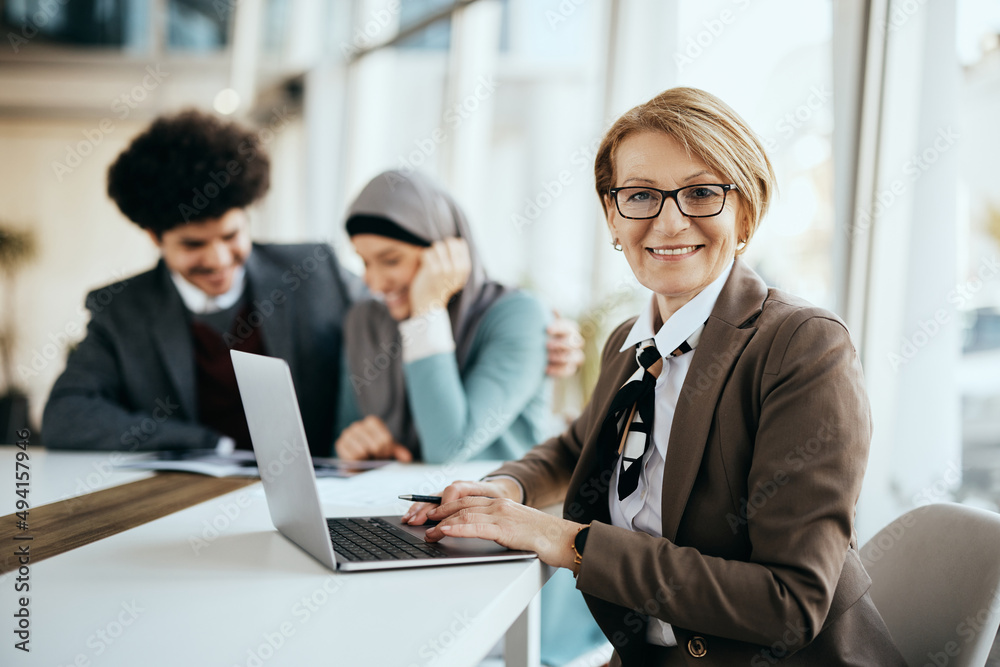 Happy senior insurance agent uses laptop while having meeting with her clients and looking at camera. Happy senior insurance agent uses laptop while having meeting with her clients and looking at camera.