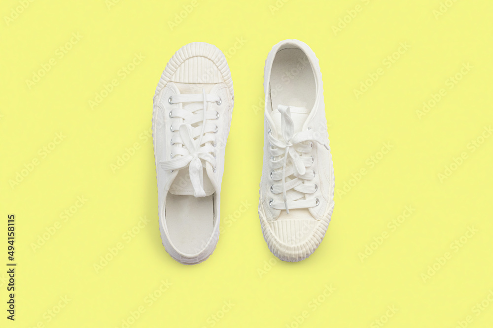 Pair of white sneakers on yellow background