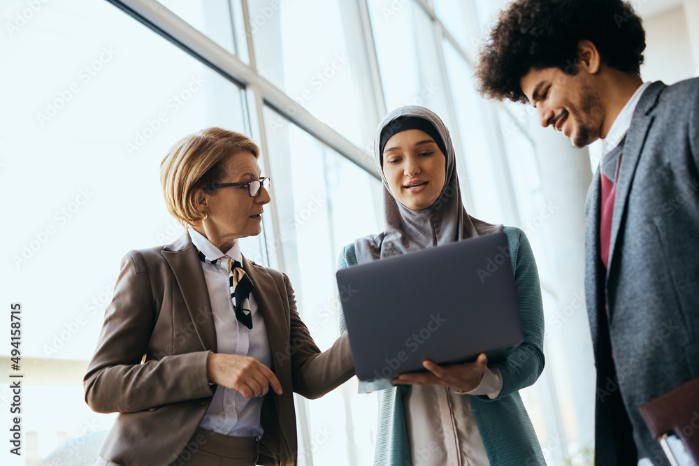 Young Muslim businesswoman and her colleagues cooperating while working on laptop.