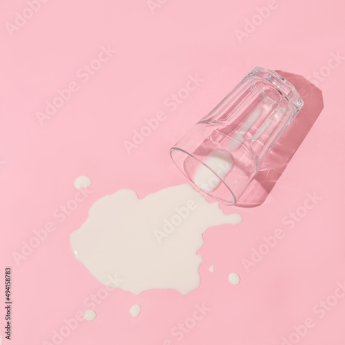 Fotografie Creative layout with  glass of spilled milk on pastel pink background