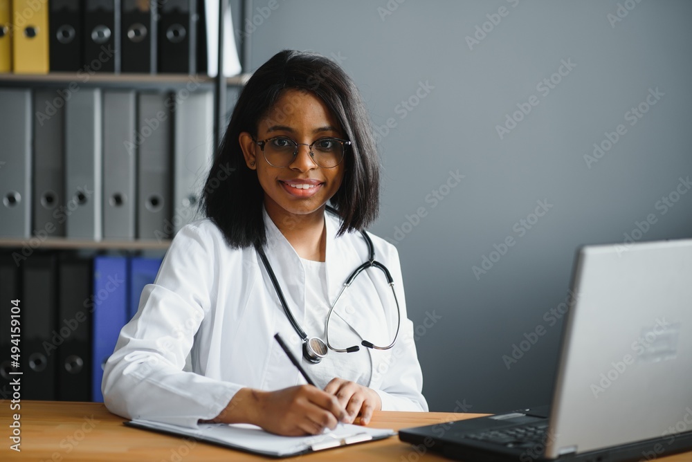 Portrait of young indian doctor working in the hospital while looking at laptop and write on clipboard Portrait of young indian doctor working in the hospital while looking at laptop and write on clipboard