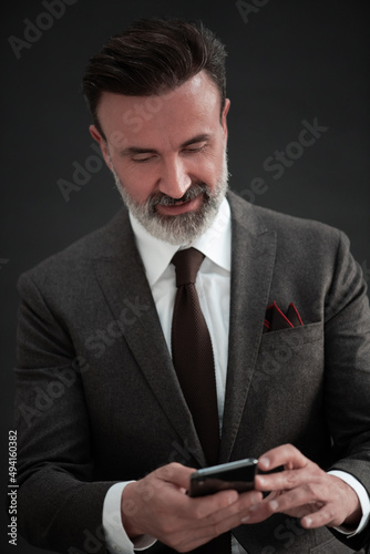 Portrait of adult businessman wearing trendy suit and sitting in modern studio on stylish chair against the black background