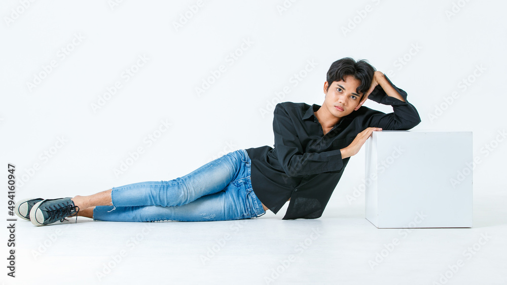 Portrait isolated cutout studio shot of Asian young LGBTQ gay glamour male model in casual black shirt and jeans outfit sitting stretching posing gesturing on floor look at camera on white background