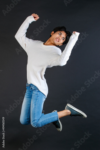 Studio shot of Asian young LGBTQ gay cheerful happy bisexual homosexual male model in casual outfit jumping high on air smiling laughing posing holding two fingers peace sign on black background photo