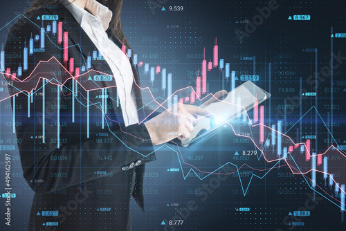 Fotografija Businesswoman hand using tablet with abstract downward forex chart on blurry dark background