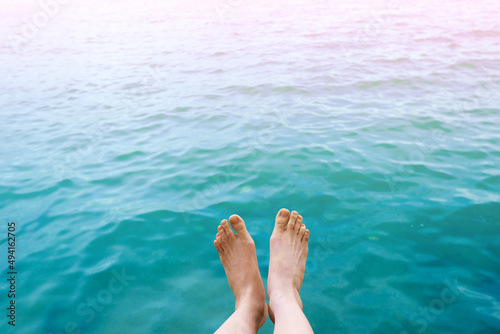 Feet top view in the aqua blue water background. Woman body legs and barefoot on summer beach.