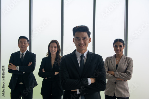 Successful businessman with crossed arms standing proudly in front his business team and looking at the camera.