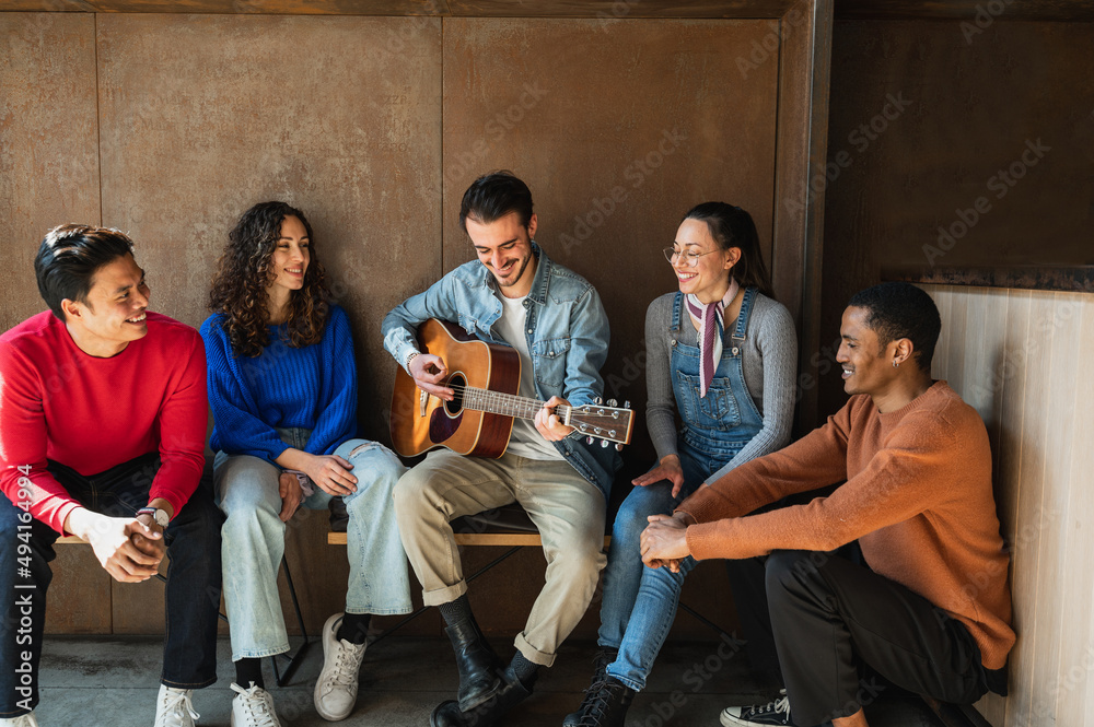 Fototapeta premium Mixed group of young friends spending time together and enjoying playing guitar and singing.