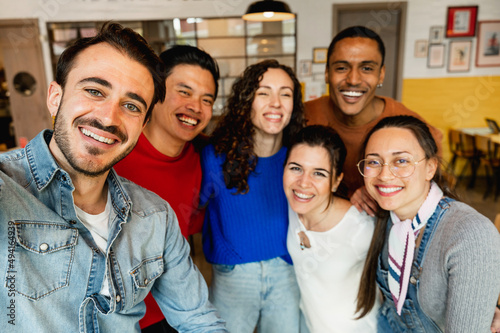 Group of six multiracial friends taking a selfie photo with smartphone in a restaurant.