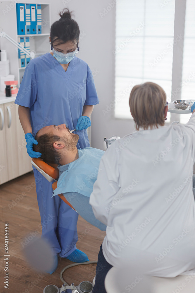 Obraz premium Dentist assistant checking patient mouth analyzing caries infection using stomatological instrument during orthodontic examination in dental office room. Concept of dentistry procedure