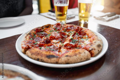 Close-up Italian pepperoni pizza on table next to glass of beer.