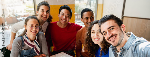 Horizontal banner or header Multiethnic group of six friends take a selfie photo in a restaurant at table while eating pizza. People with happy cheerful expression