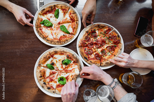 Top view three delicious Italian pizzas on table. Unrecognizable cropped people's hands taking a slice.