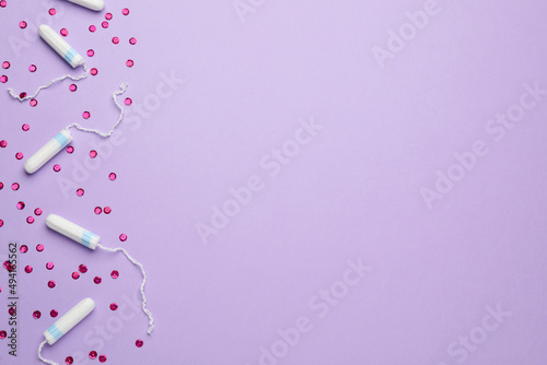 Tampons and pink sequins on violet background, flat lay with space for text. Menstrual hygiene product