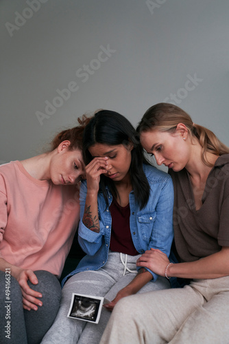 Mixed race woman holding ultrasound scan consoled by two caucasian friends