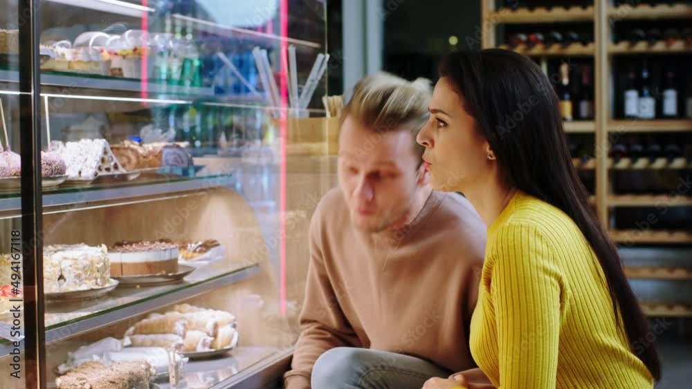 Good looking couple in the coffee shop looking at the showcase fridge woman very excited showing to her man what dessert she find