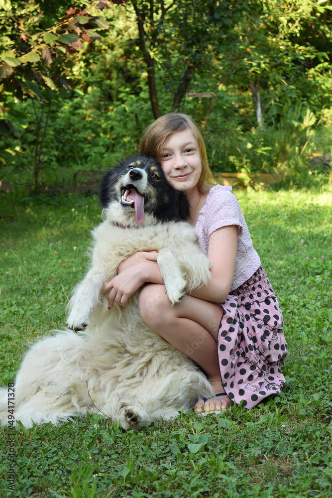 Girl playing with dog on grass. Teenager hugging Carpathian Shepherd Dog in the summer park. A Friendship concept of man and animal Girl playing with dog on grass. Teenager hugging Carpathian Shepherd Dog in the summer park. A Friendship concept of man and animal