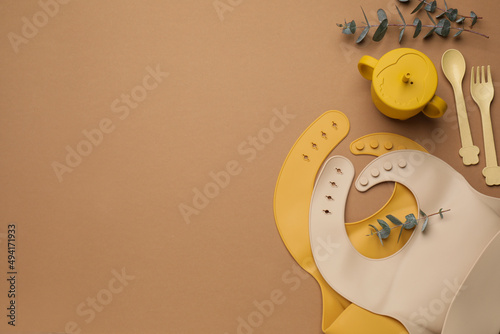 Flat lay composition with baby feeding accessories and bibs on brown background, space for text