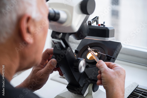 A gemologist looks at a diamond through a microscope, gemstones appraisal. gemologist holding a brilliant cut ruby and placing on the precision scale, Instruments gemologist, Craftsman appraising photo