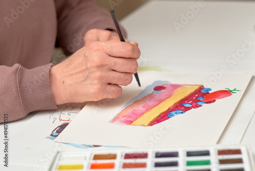 the artist's hand holds a brush and paints a cake with watercolors