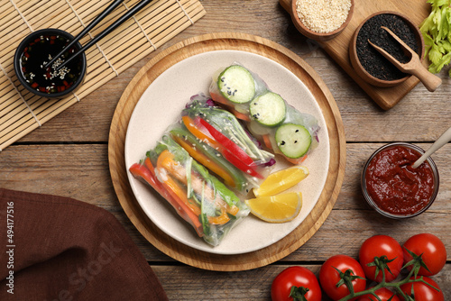 Delicious rolls wrapped in rice paper on wooden table  flat lay