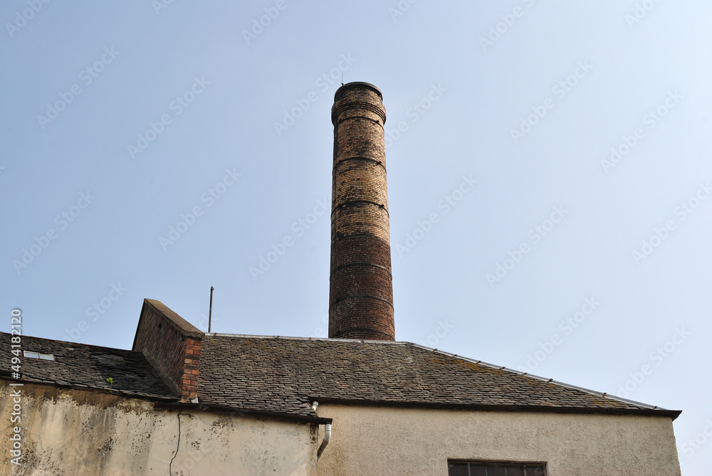 Tall Industrial Brick Chimney and Warehouse seen against Blue Sky