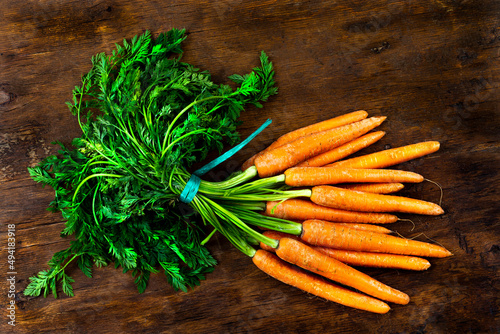 Fresh organic carrots with fane carrots bunch on rustic wooden background